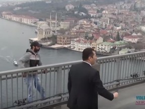 An unidentified man, left, allegedly contemplating jumping is seen on the edge of Istanbul's Bosporus Bridge. Security called the man over to Turkish President Recep Tayyip Erdogan, who had ordered his motorcade to stop in an attempt to help. (YouTube/Screengrab)
