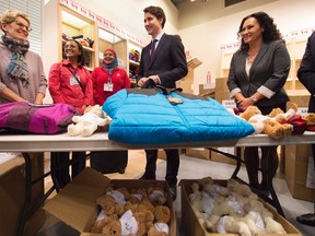 Canadian Prime Minister Justin Trudeau, second from right, and Ontario Premier Kathleen Wynne, left, look over winter clothing which will be handed out to arriving Syrian refugees before arrival at Pearson International airport, in Toronto, on Dec. 10, 2015. (THE CANADIAN PRESS/Nathan Denette)