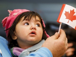 A young Syrian refugee looks up as her father holds her and a Canadian flag at the as they arrive at Pearson Toronto International Airport in Mississauga, Ontario, December 18, 2015. (REUTERS/Mark Blinch)