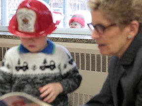 Ontario Premier Kathleen Wynne reads to Jacob Claessen, 2, while Duncan Kerry, 2, looks in from the outside at the child care centre at the YMCA of Kingston, Jan. 19, 2015. Wynne was in Kingston to announce a planned raise to the wages paid to child care workers. (Elliot Ferguson/Kingston Whig-Standard/Postmedia Network)