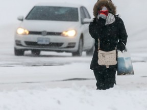 A woman covers her face as she walks along Strandherd Drive during the first major snow fall of the season in Ottawa on Tuesday December 29, 2015. Errol McGihon/Ottawa Sun/Postmedia Network