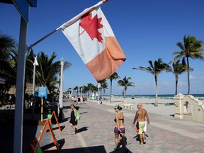 A Canadian flag flies as people walk along the boardwalk in Hollywood, Fla. in November. Visits by the United States' largest supply of international visitors from Canada are expected to be down by eight percent this year due to the weak Canadian dollar. (AP Photo/Lynne Sladky)