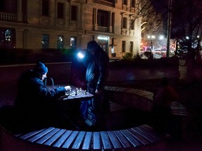 In this Sunday, Dec. 27, 2015 photo people play chess holding a flashlight near Nakhimov's Square in Sevastopol, Crimea. As New Year’s Eve approaches, the central square of Crimea’s largest city is festooned with lighted holiday decorations, including a soaring artificial tree that flashes and winks. But areas a few steps away are sunk in darkness, the streetlamps turned off because of an electricity shortage. (AP Photo/Alexander Polegenko)