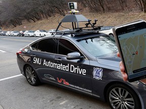 A researcher from the Intelligent Vehicle IT Research Center at Seoul National University shows the smartphone application for the driverless car called Snuber with a fixture on its roof with devices that scan road conditions at Seoul National University’s campus in Seoul, South Korea, Tuesday, Jan. 5, 2016. (AP Photo/Lee Jin-man)