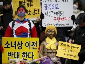 People hold placards next to a statue symbolizing "comfort women" during a weekly anti-Japan rally in front of Japanese embassy in Seoul, South Korea, December 30, 2015. The placard (bottom L) reads, "Oppose the relocation of the statue." REUTERS/Kim Hong-Ji