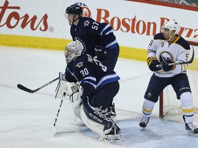 Buffalo Sabres forward Evander Kane sits in the crease behind Winnipeg Jets goaltender Connor Hellebuyck as Tyler Myers (left) defends in Winnipeg on Sun., Jan. 10, 2016. (Kevin King/Winnipeg Sun/Postmedia Network)