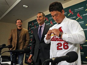 New Cardinals relief pitcher Seung Hwan Oh puts on his new jersey on Monday, Jan. 11, 2016, during a news conference as Cardinals manager Mike Matheny, left, and Senior VP and GM John Mozeliak look on, at Busch Stadium, in St. Louis. (J.B. Forbes/St. Louis Post-Dispatch via AP)