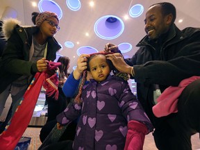 Kinda (centre) is fitted for a parka and tuque by Abdikheir Ahmed (right) of Immigration Partnership Winnipeg after arriving at the Winnipeg James Armstrong Richardson International Airport from Saudi Arabia with 10 siblings on Thursday. (Kevin King/Winnipeg Sun/Postmedia Network)