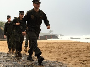 U.S. Marines walk on the beach at Waimea Bay near Haleiwa, Hawaii, where two military helicopters crashed into the ocean about 2 miles offshore, Friday, Jan. 15, 2016. The helicopters carrying 12 crew members collided off the Hawaiian island of Oahu during a nighttime training mission, and rescuers are searching a debris field in choppy waters Friday, military officials said. (Mariana Keller via AP Photo)