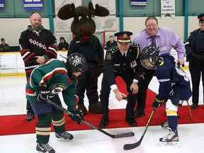 John Lappa/Sudbury Star
Greater Sudbury Police Chief Paul Pedersen, middle, and Dalton Wilcox, left, of the Westmount Wolverines, and Thomas Arseneault, of the Lo-Ellen Lightning, take part in an official puck drop to launch the Greater Sudbury Police Service 2016 Police Cup at the Gerry McCrory Countryside Sports Complex on Friday, as Brian MacRury, back left, of the Sudbury Police Association, Dan Xilon, executive director of the Sudbury Food Bank, and Sgt. Anita Hass, of the Greater Sudbury Police, look on. Participants and spectators are encouraged to donate money or non-perishable food items at Countryside, Cambrian and Carmichael arenas where the tournament is being played. The money and food will be donated to the Sudbury Food Bank. A total of 500 players from 31 teams in the Sudbury Playground Hockey League are participating in the tournament which wraps up on Sunday.