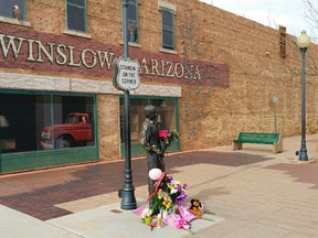 In this Tuesday, Jan. 19, 2016, photo courtesy of Tom McCauley, the corner in Winslow, Ariz., made famous by the 1972 Eagles' song "Take it Easy." Fans are leaving flowers, hand-written notes and candles at the site to celebrate the life of Eagles band member Glenn Frey. Frey died Monday, Jan. 18. He was 67. (Tom McCauley via AP)