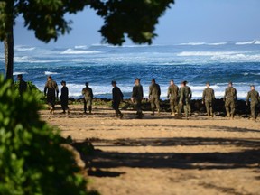 A group of Marines walk the beach outside the Haleiwa Incident Command Post in Haleiwa, Hawaii, during search efforts for 12 missing Marines, in this handout photo taken January 18, 2016. The U.S. Coast Guard said on Tuesday it had suspended its search for 12 Marines who have been missing since two military helicopters collided last week off Hawaii's Oahu island.  Picture taken January 18, 2016. REUTERS/U.S. Coast Guard/Petty Officer 1st Class Levi Read/Handout via Reuters