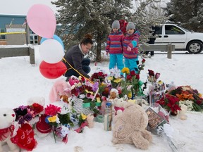 Tashina Montgrand lays flowers outside the La Loche Community School as her daughters Tayala and Tayvah look on in La Loche, Sask., Monday, Jan. 25, 2016. A seventeen-year-old youth allegedly shot two people at the school last Friday after shooting two brothers to death earlier at a home nearby. THE CANADIAN PRESS/Jonathan Hayward