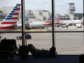 A traveller rests on the floor as American Airlines aircraft are lined up the the gates at Miami International Airport, Tuesday, Nov. 24, 2015, in Miami. (AP Photo/Lynne Sladky)