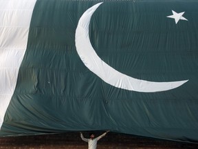A man adjusts a Pakistani flag on a building. FILE pic. (REUTERS/Mohsin Raza)