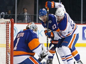 Edmonton Oilers left wing Benoit Pouliot fights for the puck in front of New York Islanders goalie Thomas Greiss while working around the defence of Islanders center Anders Lee in New York on Sunda(Kathy Willens/AP)