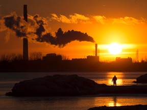 A man photographs the setting sun as powerplant smokestacks battle freezing temperatures in Toronto on Friday, January 16, 2015. THE CANADIAN PRESS/Frank Gunn