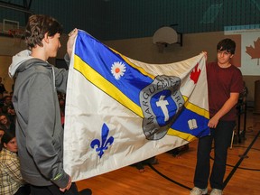 Grade 8 students Lucas Wimmer, left, and Sam Mitchell-McAdoo reveal the new school flag to the students, teachers and guests during a morning assembly at St. Marguerite Bourgeoys Catholic School in Kingston on Friday. The design, by Grade 8 student Tyeson Hunt, was chosen from hundreds submitted by the students as a way to represent the school. (Julia McKay/The Whig-Standard)