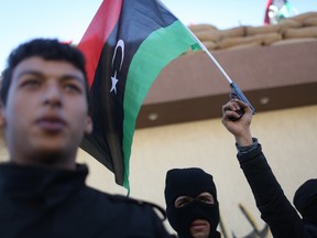Libyan security forces stand in front of the security headquarters, one showing his weapon with a Libyan flag, in Sabratha, Libya, Saturday, Feb. 20, 2016. (AP Photo/Mohamed Ben Khalifa)