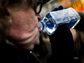 Michael Moore drinks from a Fiji water bottle accompanied by dozens of Flint, Mich. residents as he accuses Gov. Rick Snyder of poisoning the city's water during a rally Jan. 16, 2016. (THE CANADIAN PRESS/AP/Jake May/The Flint Journal - MLive.com via AP)
