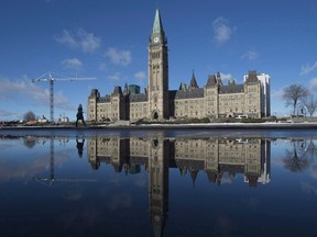 The centre block of the Parliament buildings is reflected in a puddle as a woman walks past, in Ottawa on February 1, 2016. The Canadian Taxpayers Federation is criticizing the federal government for quietly approving a $25m increase to MPs' office budgets. THE CANADIAN PRESS/Adrian Wyld