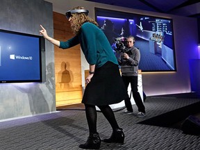 In this Jan. 21, 2015, file photo, Microsoft's Lorraine Bardeen demonstrates the HoloLens headset as what she "sees" is projected on a screen behind at an event at the company's headquarters in Redmond, Wash. (AP Photo/Elaine Thompson, File)