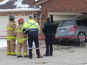 Firefighters, a paramedic and a police officer survey the damage to a garage after a SUV crashed through its doors on Kanata Crescent in London on Thursday. Craig Glover/The London Free Press/Postmedia Network