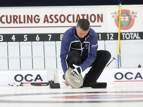 Skip Wayne Middaugh wipes ice from the bottom of a rock before throwing during his match against Team Kean at the Ontario Curling Championships at the Flight Exec Centre in Dorchester, Ont., on Feb. 5, 2015. (CRAIG GLOVER/The London Free Press)