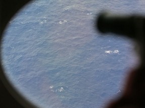 In this Tuesday, April 1, 2014, file photo, an observer on a Japan Coast Guard Gulfstream aircraft takes photos out of a window while searching for the missing Malaysia Airlines Flight MH370 in the Southern Indian Ocean, near Australia.  (AP Photo/Rob Griffith, Pool)