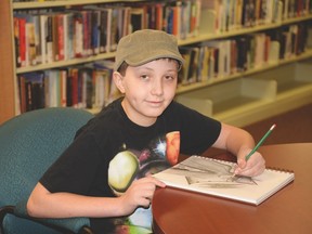 Duncan Mackay shades in a comic book hero in his sketchbook at the Stony Plain Public Library. The young artist is lending his skills to the library in creating a comic book that will be used to teach about misinformation found online. - Photo by Marcia Love