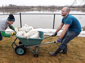 Volunteers Brett Radford (l) and Palmer Rouse move a cart full of sandbags while helping to construct a dike on Lord Avenue in Winnipeg Saturday April 9, 2011.