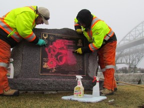 Doug Moore, left, and Rob Woods, with the Blue Water Bridge, remove graffiti from a memorial to Robert Campbell near the bridge Tuesday in Point Edward. The memorial, and other areas of the waterfront, were defaced on the weekend with graffiti. (Paul Morden, Sarnia Observer)