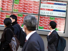 People walk past an electronic stock board showing Japan's Nikkei 225 at a securities firm in Tokyo Tuesday, March 22, 2016. (AP Photo/Eugene Hoshiko)