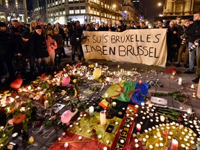 People holding a banner reading "I am Brussels" behind flowers and candles to mourn for the victims at Place de la Bourse in the center of Brussels, Tuesday, March 22, 2016. Bombs exploded at the Brussels airport and one of the city's metro stations Tuesday, killing and wounding scores of people, as a European capital was again locked down amid heightened security threats. (AP Photo/Martin Meissner)
