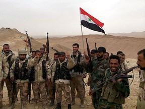 Forces loyal to Syria's President Bashar al-Assad flash victory signs and carry a Syrian national flag on the edge of the historic city of Palmyra in Homs Governorate, in this handout picture provided by SANA on March 26, 2016. REUTERS/SANA/Handout