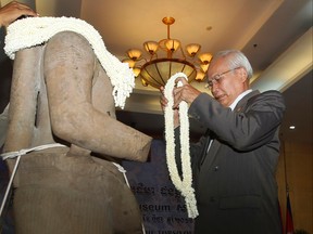 Cambodia's Secretary of State for the Ministry of Culture and Fine Arts Chuch Phoeun holds a bundle of jasmine to place onto the Torso of Rama, a 10th century stone statue, during a handing over ceremony in Phnom Penh, Cambodia, Monday, March 28, 2016. Cambodia welcomed home the stone statue, that was looted from a temple during the country's civil war, from Denver Art Museum in the United States. (AP Photo/Heng Sinith)