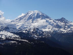 In this file photo taken June 19, 2013, Mount Rainier is seen from a helicopter flying south of the mountain and west of Yakima, Wash. One climber has likely died from hypothermia and exposure on Mount Rainier after he and his climbing partner were caught in a winter storm over the weekend, a spokeswoman with Mount Rainier National Park said. A Chinook helicopter crew and other rescue teams were working Monday, March 28, 2016, to reach the 58-year-old man from Norway. (AP Photo/Elaine Thompson, File)