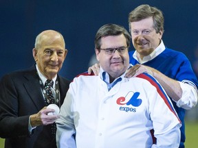 Montreal Mayor Denis Coderre limbers up with the help of Toronto Mayor John Tory prior to throwing a ceremonial pitch during a pre-game ceremony, Saturday, April 2, 2016 in Montreal. Handing over the ball in former Montreal Expos owner Charles Bronfman. THE CANADIAN PRESS/Paul Chiasson