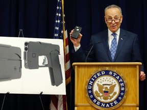 Standing beside photographs of a new product, U.S. Sen Charles Schumer, shown holding an iPhone 5S, voices his opposition to a handgun that appears to be a cell phone during a news conference in his office, Monday, April 4, 2016, in New York. (AP Photo/Kathy Willens)