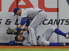 Blue Jays right fielder Michael Saunders (top) checks in on Kevin Pillar after the centre fielder made an incredible leaping catch before crashing head-first into the wall in Tampa on Monday night. (The Associated Press)
