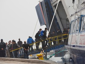 An officer from the European Union’s border protection agency, Frontex, leads a migrant to board a ferry in the port of Mytilini, Lesbos island , Greece, on Friday, April 8, 2016. (AP Photo/Petros Giannakouris)