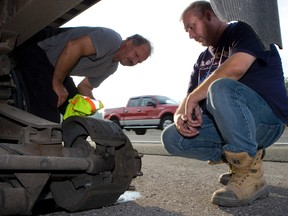 A tow operator and the driver of the transport (right) look at where the set of dual wheels came off the transport on Highway 401. (Postmedia Network file photo)