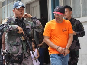 In this Friday, June 20, 2014 file photo, a Philippine police officer escorts Abu Sayyaf extremist group leader Khair Mundos, right, after his arraignment at courts inside a police camp in Taguig City, south of Manila, Philippines. Abu Sayyaf, the Philippines militant group responsible for killing a Canadian hostage on Monday, sprang up in the early 1990s as an offshoot of another, larger Islamic insurgent group.THE CANADIAN PRESS/AP/Mark Cristino