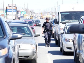 Constable Andrew Hinds, of the Greater Sudbury Police traffic management unit, walks between vehicles stopped at a traffic light on Lasalle Boulevard looking for distracted drivers in Sudbury, Ont. on Wednesday April 27, 2016. Gino Donato/Sudbury Star/Postmedia Network