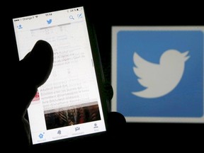 A man reads tweets on his phone in front of a displayed Twitter logo in Bordeaux, southwestern France, March 10, 2016. REUTERS/Regis Duvignau/Illustration/File Photo