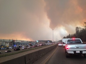 Smoke fills the air as cars line up on a road in Fort McMurray, Alberta on Tuesday May 3, 2016. At least half of the city of Fort McMurray in northern Alberta was under an evacuation notice Tuesday as a wildfire whipped by winds engulfed homes and sent ash raining down on residents. (THE CANADIAN PRESS/Greg Halinda)