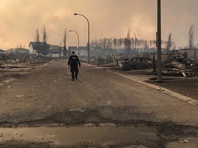 An RCMP officer surveys the damage on a street in Fort McMurray, Alta. in a photo from the RCMP Alberta Twitter feed. A wildfire that has devastated parts of Fort McMurray has exploded in size, and officials say they are now water bombing the city to keep it from being overwhelmed by flames.THE CANADIAN PRESS/HO-Twitter-RCMP Alberta MANDATORY CREDIT