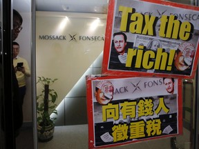 Security guards are reflected by a door where  placards featuring the portraits of Chinese Communist Party leader Xi Jinping and British Prime Minister David Cameron are displayed by protesters, at the entrance of the regional head office of Panama-based law firm Mossack Fonseca in Hong Kong, Tuesday, April 12, 2016. (AP Photo/Kin Cheung)
