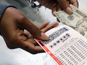 In this Jan. 13, 2016 file photo, a clerk hands over a Powerball ticket for cash at Tower City Lottery Stop in Cleveland. (AP Photo/Tony Dejak, File)