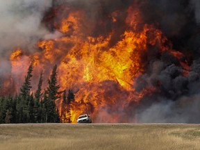 Smoke and flames from the wildfires erupt behind a car on the highway near Fort McMurray, Alberta, Canada, May 7, 2016. REUTERS/Mark Blinch